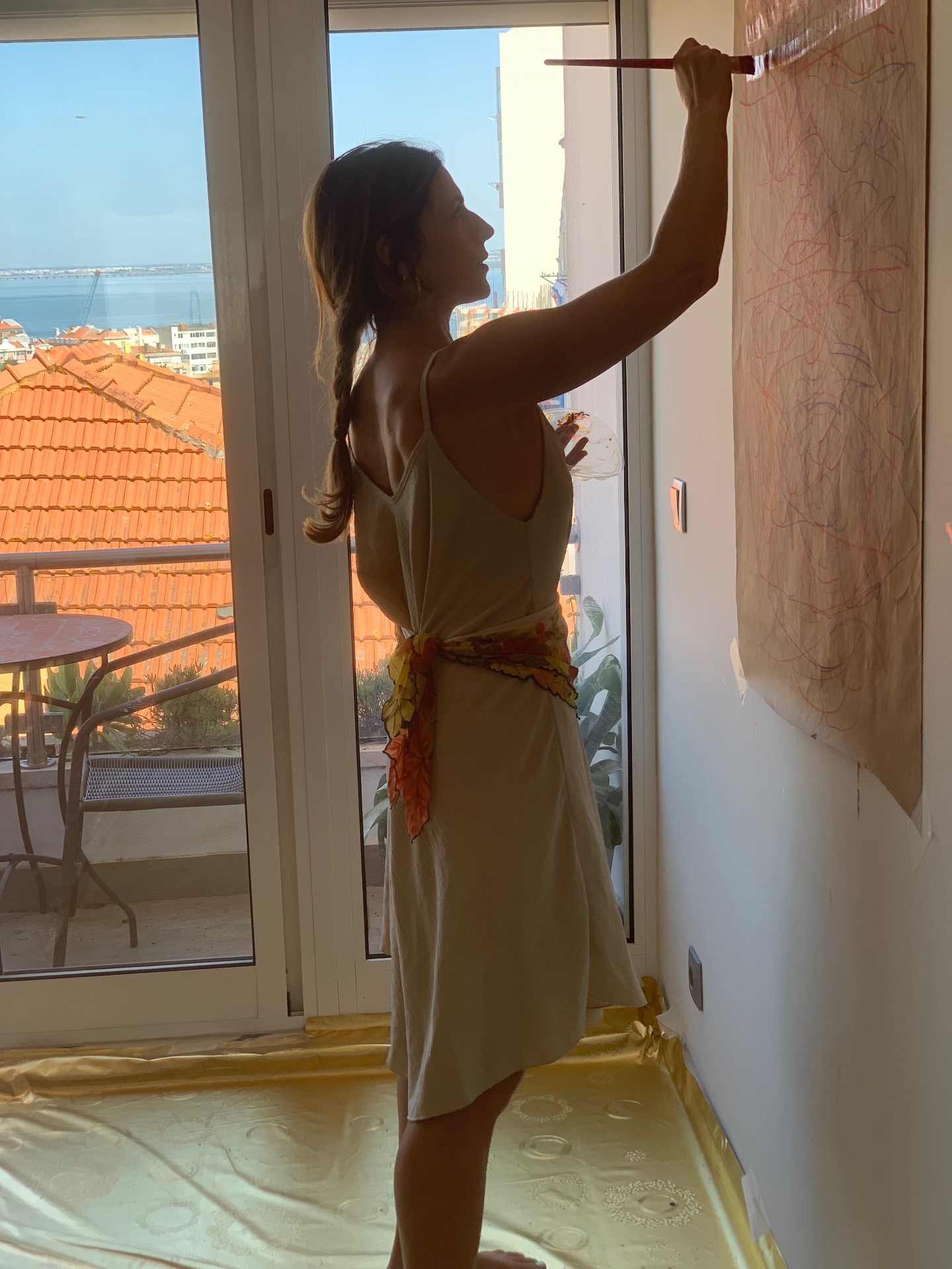 Painting on brown craft paper taped to the studio wall, with the river Tejo visible through the window